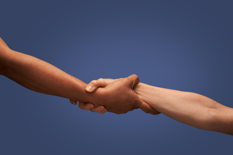 Two people's arms grabbing each other by the wrist as if helping someone up.