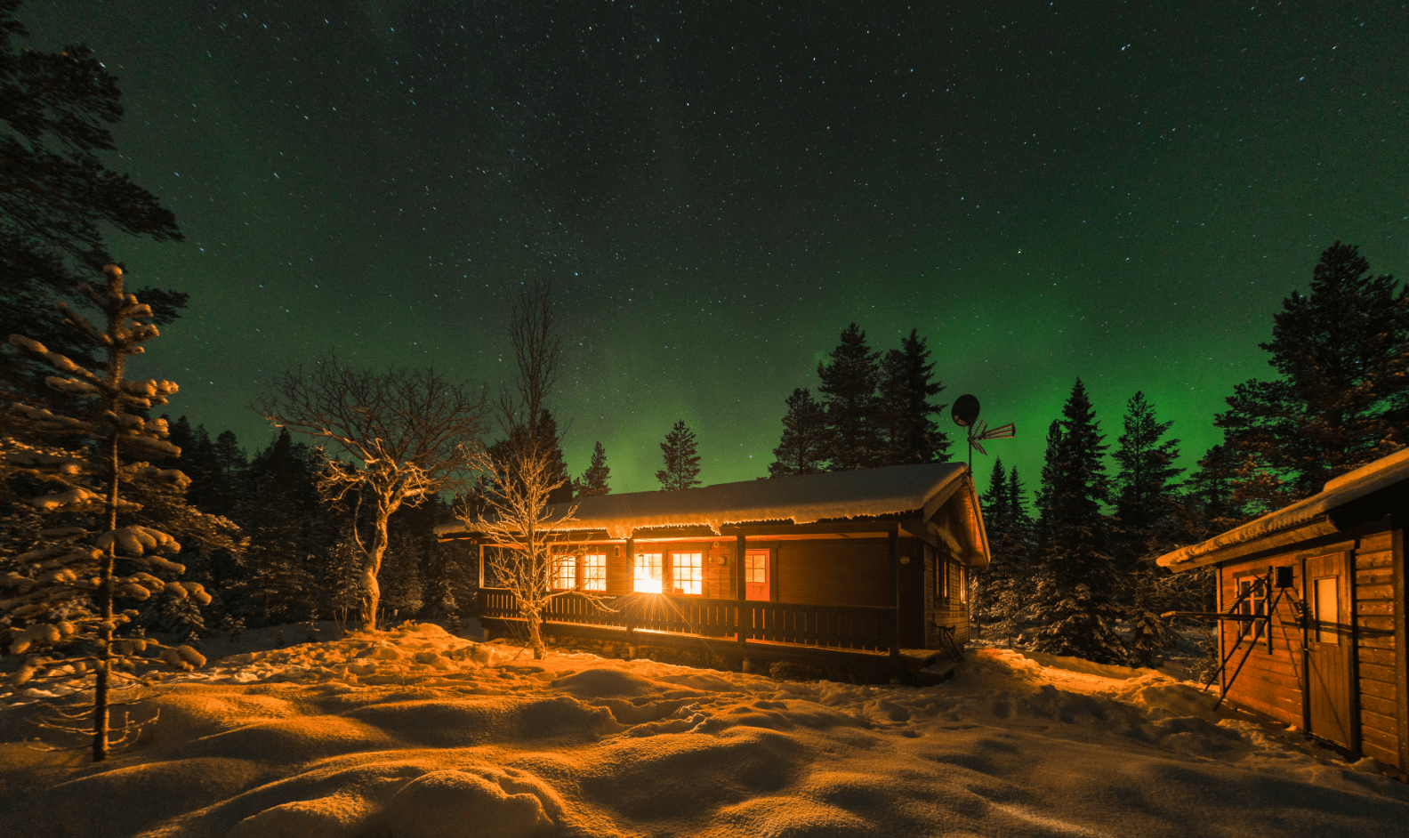 A lit up cabin in snowy woods at night.